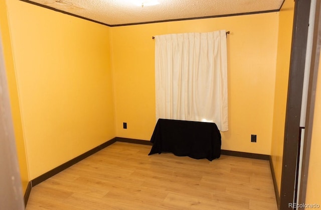 spare room featuring light hardwood / wood-style floors, a textured ceiling, and ornamental molding