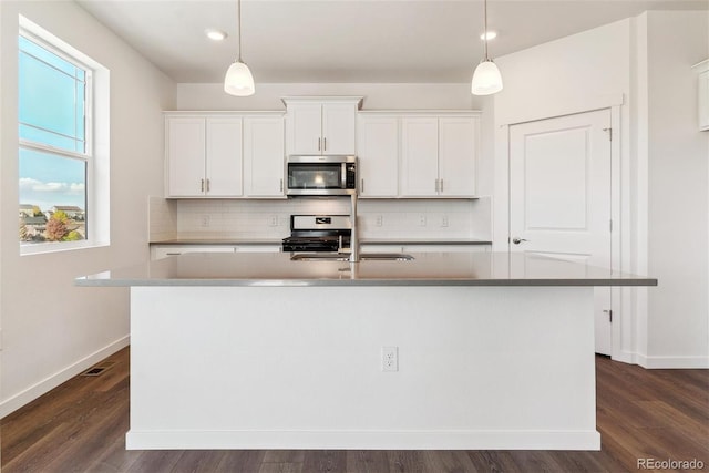 kitchen with stainless steel appliances, dark wood-type flooring, a center island with sink, white cabinets, and hanging light fixtures