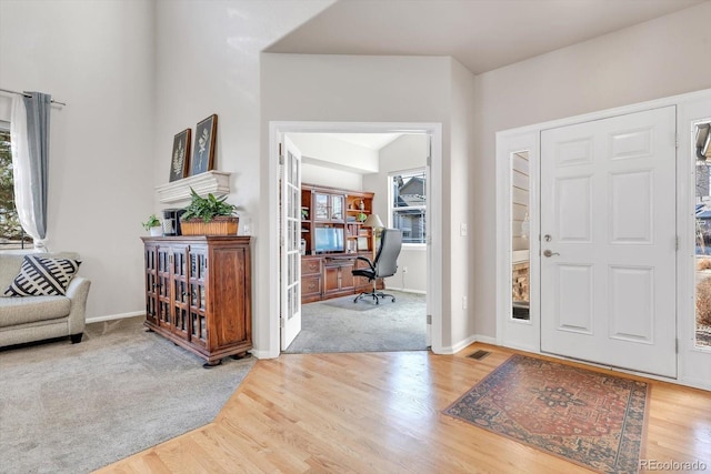 carpeted foyer featuring baseboards, visible vents, and wood finished floors