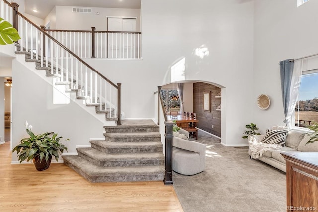 interior space featuring wood finished floors, stairway, a towering ceiling, and visible vents