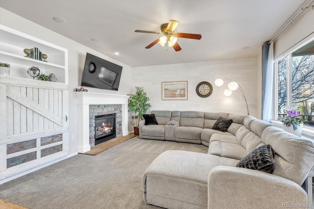 living room with built in shelves, a glass covered fireplace, ceiling fan, and carpet