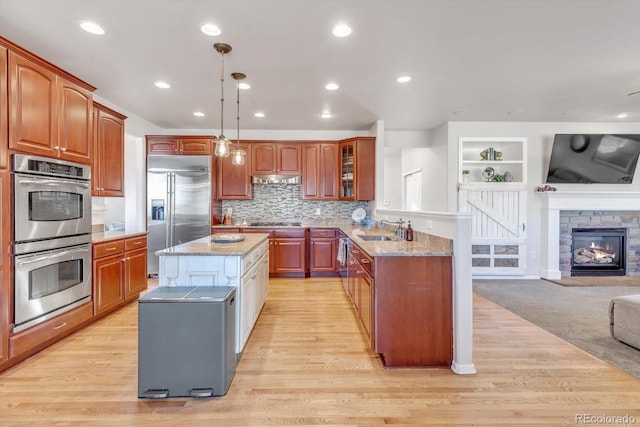 kitchen with open floor plan, stainless steel appliances, light stone counters, and a sink