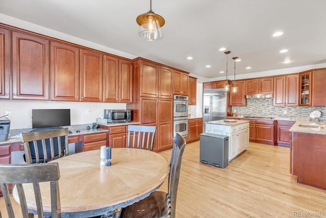 kitchen featuring glass insert cabinets, a center island, stainless steel appliances, light wood-type flooring, and under cabinet range hood