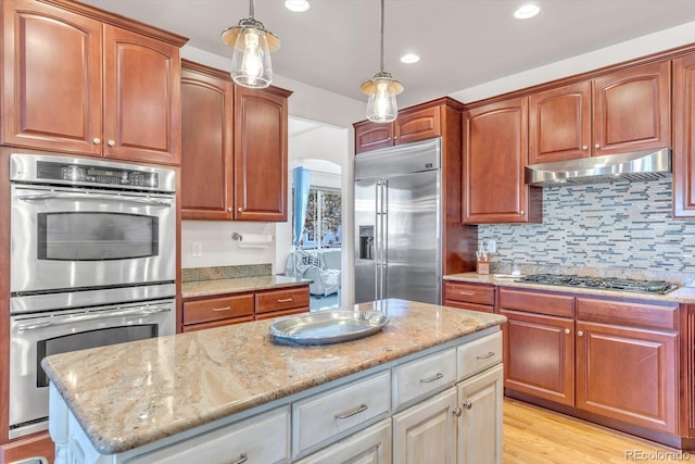 kitchen featuring decorative light fixtures, appliances with stainless steel finishes, light stone countertops, and under cabinet range hood