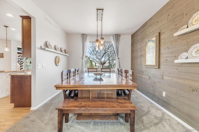 dining area with light carpet, wooden walls, visible vents, an accent wall, and a notable chandelier