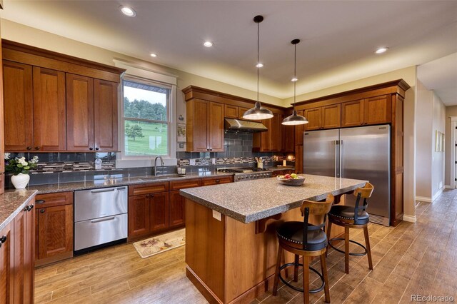 kitchen with a kitchen island, decorative light fixtures, sink, stainless steel appliances, and light hardwood / wood-style flooring