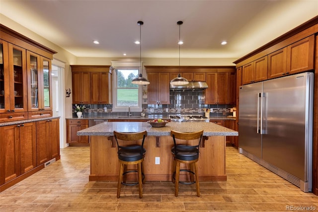 kitchen featuring stainless steel built in refrigerator, tasteful backsplash, a kitchen breakfast bar, a kitchen island, and pendant lighting