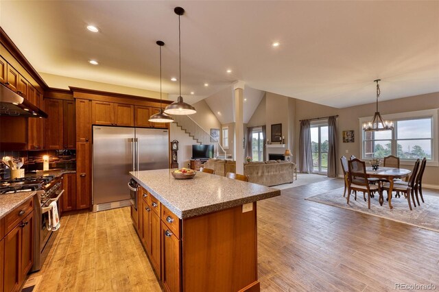 kitchen with light stone counters, high quality appliances, a kitchen island, and hanging light fixtures