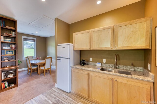 kitchen featuring light stone counters, sink, white fridge, and light brown cabinets