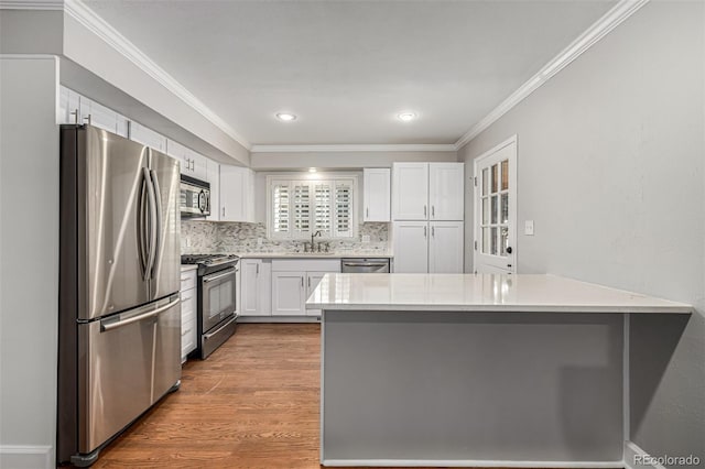 kitchen with white cabinetry, sink, hardwood / wood-style flooring, appliances with stainless steel finishes, and ornamental molding