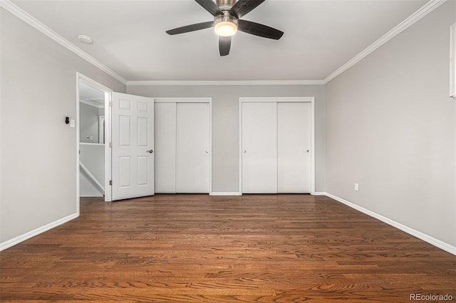 unfurnished bedroom with ceiling fan, crown molding, dark wood-type flooring, and two closets