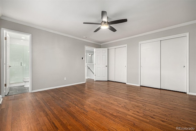 unfurnished bedroom with connected bathroom, ceiling fan, dark wood-type flooring, two closets, and ornamental molding