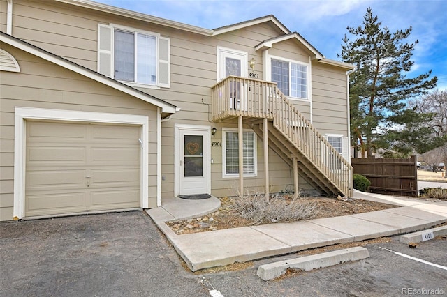 townhome / multi-family property featuring an attached garage, stairway, driveway, and fence