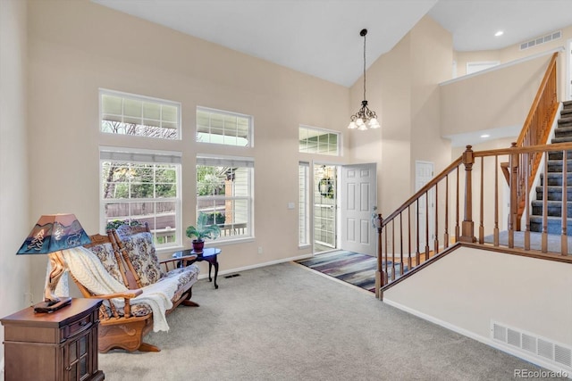 carpeted foyer featuring a notable chandelier, stairs, baseboards, a towering ceiling, and visible vents