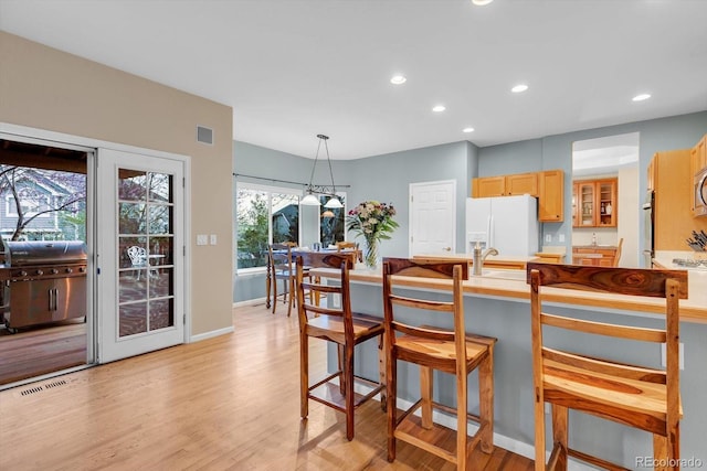 kitchen with recessed lighting, a kitchen breakfast bar, white fridge with ice dispenser, and light wood-type flooring