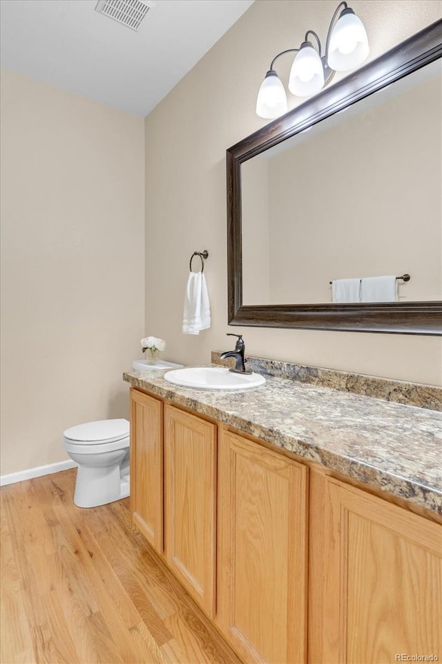 bathroom featuring visible vents, wood finished floors, vanity, baseboards, and toilet
