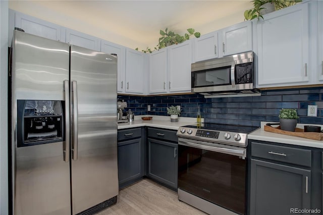 kitchen with gray cabinets, white cabinets, decorative backsplash, stainless steel appliances, and light hardwood / wood-style flooring