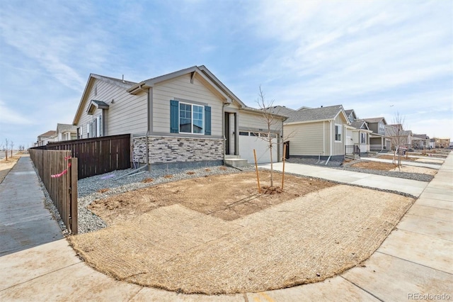 ranch-style house featuring an attached garage, fence, stone siding, and driveway