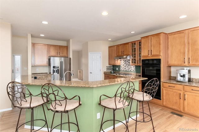 4814 S Upham Ct, Littleton, CO 80123 - kitchen with appliances with stainless steel finishes, under cabinet range hood, a kitchen bar, light wood-type flooring, and recessed lighting