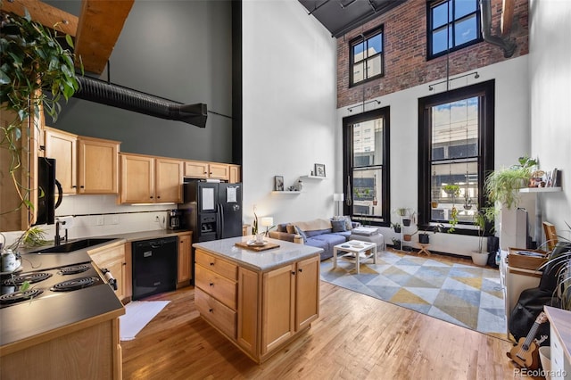 kitchen featuring light brown cabinetry, a high ceiling, a sink, open floor plan, and black appliances
