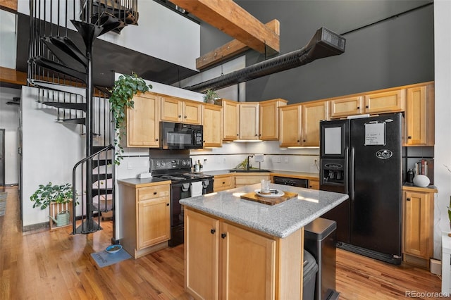 kitchen with a towering ceiling, a sink, black appliances, light wood finished floors, and light brown cabinets
