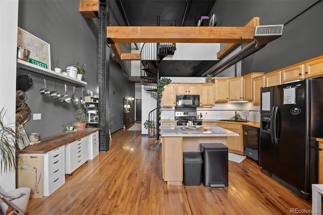 kitchen with a center island, a sink, black appliances, light brown cabinets, and a high ceiling