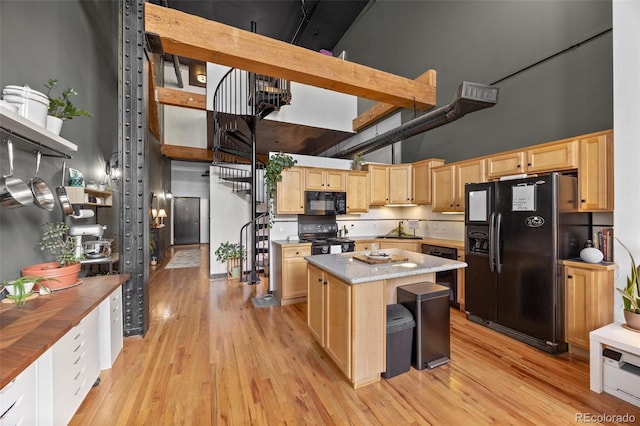 kitchen with a high ceiling, a sink, light brown cabinets, a kitchen island, and black appliances