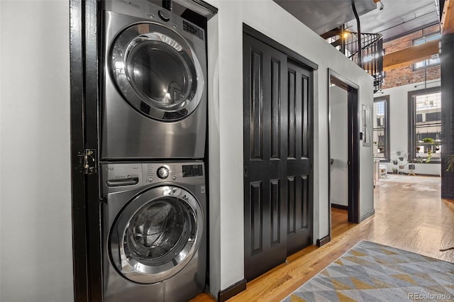 clothes washing area featuring stacked washer / drying machine, wood finished floors, and laundry area