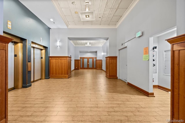 hall featuring elevator, baseboards, wainscoting, and light wood-type flooring