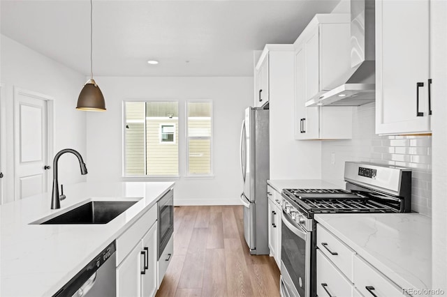 kitchen with wall chimney exhaust hood, sink, white cabinetry, decorative light fixtures, and appliances with stainless steel finishes