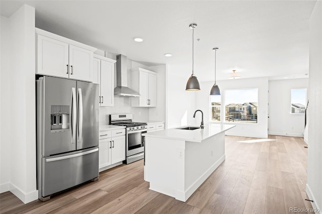 kitchen featuring wall chimney exhaust hood, sink, white cabinetry, appliances with stainless steel finishes, and an island with sink