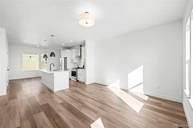 kitchen featuring wall chimney exhaust hood, white cabinetry, hanging light fixtures, an island with sink, and stainless steel appliances