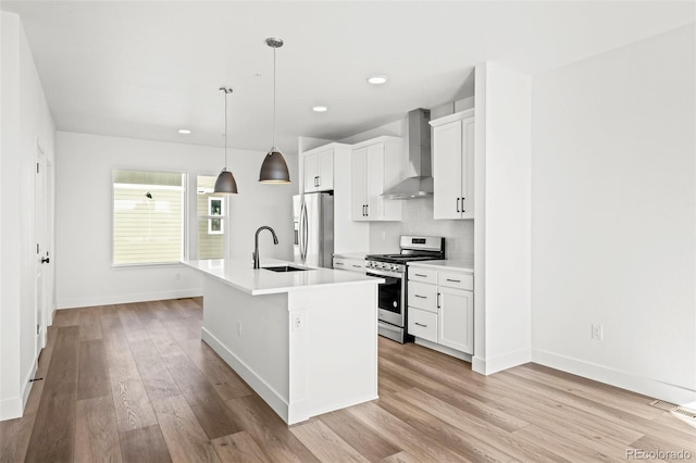 kitchen featuring wall chimney exhaust hood, sink, a center island with sink, appliances with stainless steel finishes, and pendant lighting