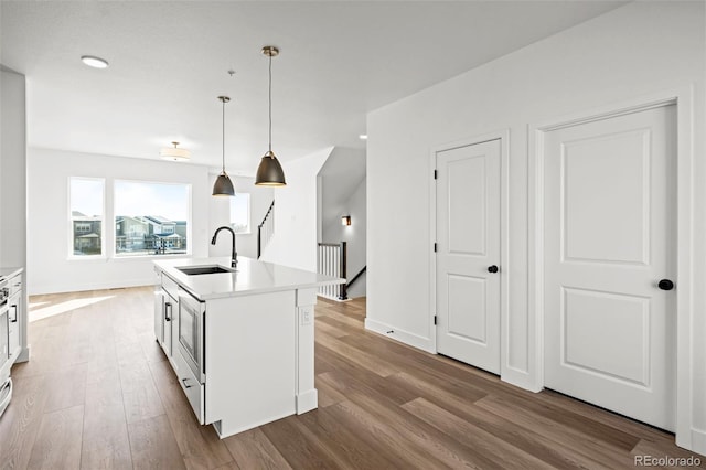 kitchen with sink, decorative light fixtures, an island with sink, light hardwood / wood-style floors, and white cabinets