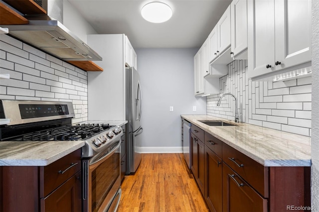 kitchen with wall chimney exhaust hood, appliances with stainless steel finishes, a sink, and white cabinets