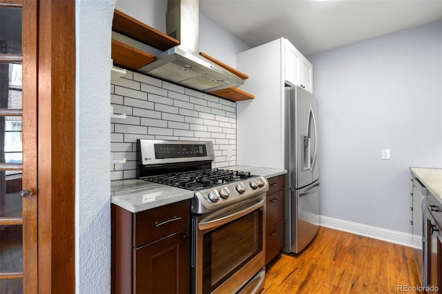 kitchen with light wood finished floors, tasteful backsplash, baseboards, island exhaust hood, and stainless steel appliances