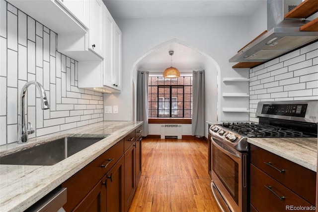 kitchen with a sink, wall chimney range hood, appliances with stainless steel finishes, open shelves, and radiator heating unit