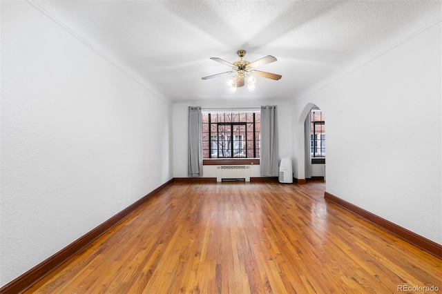 empty room with arched walkways, radiator, a ceiling fan, baseboards, and hardwood / wood-style flooring