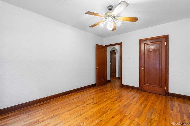 unfurnished bedroom with light wood-type flooring, arched walkways, ceiling fan, and baseboards