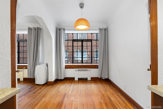 unfurnished room with baseboards, light wood-style flooring, and radiator heating unit