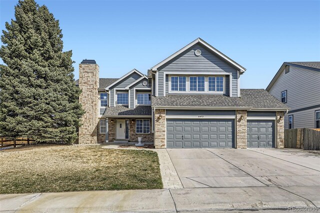 traditional-style home with a chimney, concrete driveway, roof with shingles, and fence