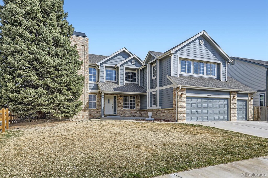 view of front facade featuring brick siding, a shingled roof, a front yard, a garage, and driveway