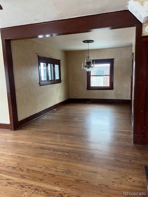 unfurnished dining area featuring dark hardwood / wood-style flooring, a notable chandelier, beam ceiling, and plenty of natural light