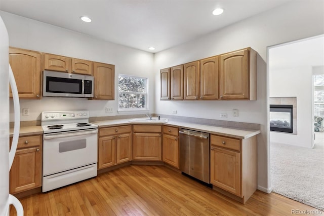 kitchen featuring stainless steel appliances, sink, a fireplace, and light hardwood / wood-style flooring