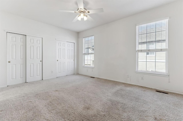 unfurnished bedroom featuring multiple closets, ceiling fan, and carpet floors