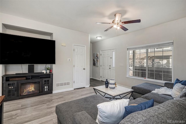 living room featuring wood finished floors, visible vents, baseboards, ceiling fan, and a glass covered fireplace