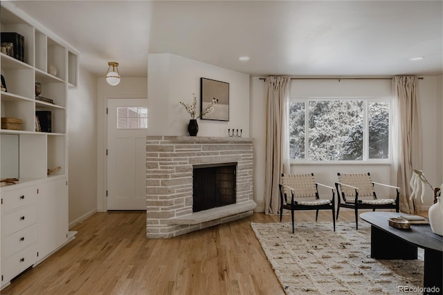 sitting room featuring a stone fireplace, light hardwood / wood-style flooring, and plenty of natural light