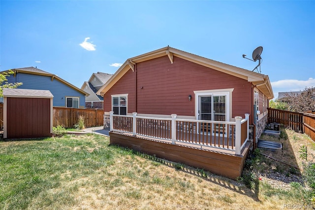 rear view of property featuring a yard, a deck, and a storage unit