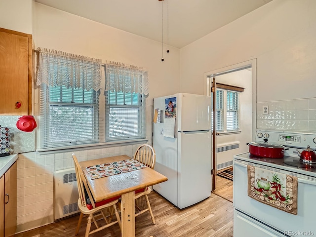 kitchen featuring decorative backsplash, radiator heating unit, light hardwood / wood-style floors, and white appliances