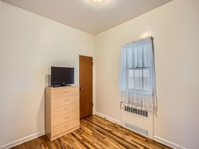 unfurnished bedroom featuring radiator heating unit and hardwood / wood-style flooring